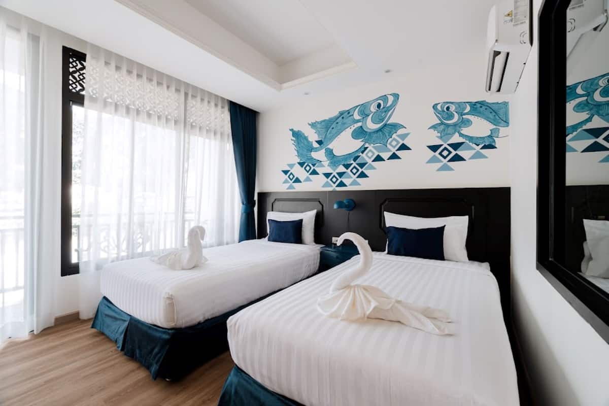 Habitación de hotel con dos camas, cada una con almohada con forma de cisne, ropa de cama blanca y un diseño geométrico en la pared.