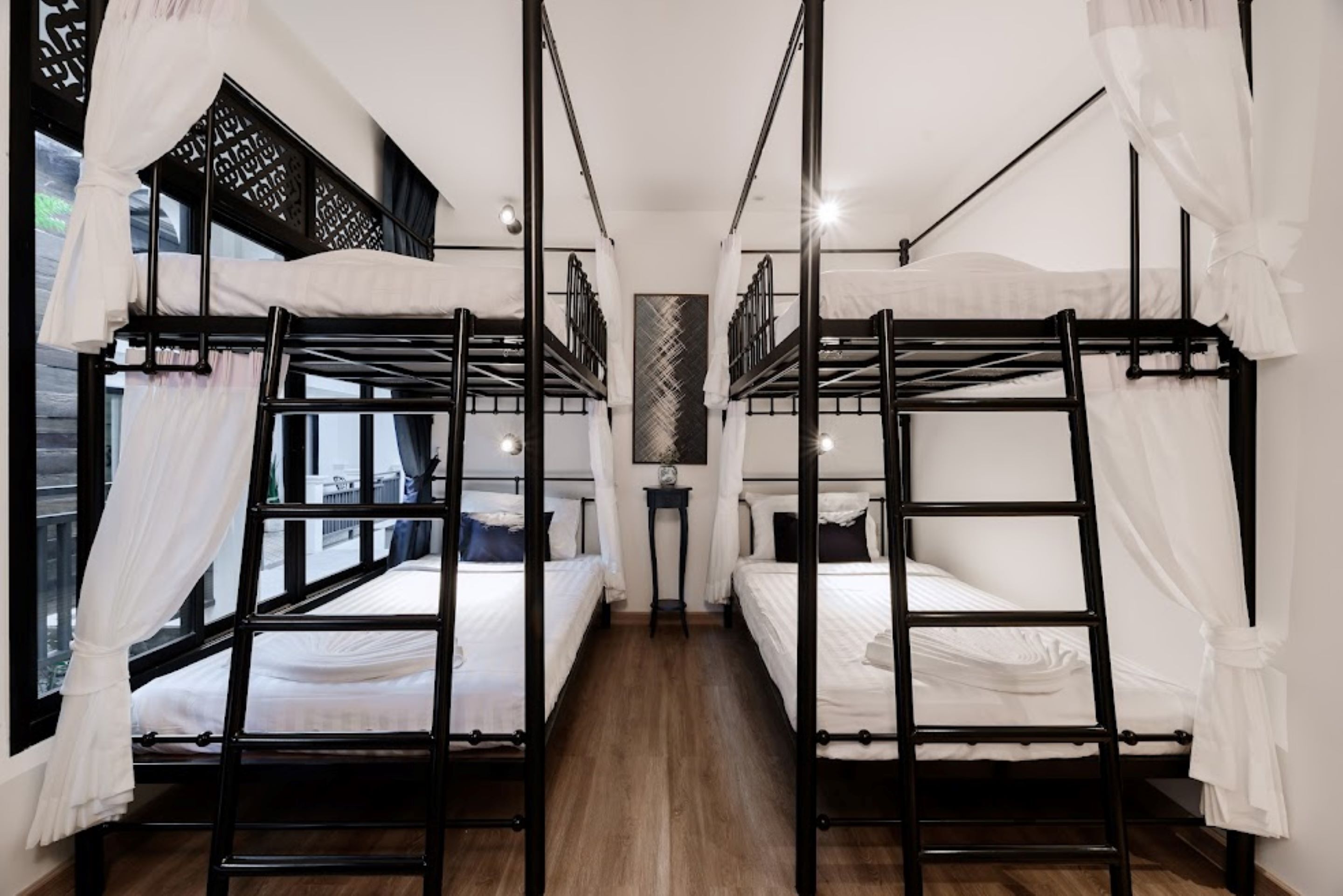 Una habitación con literas, ropa de cama blanca y cortinas translúcidas.