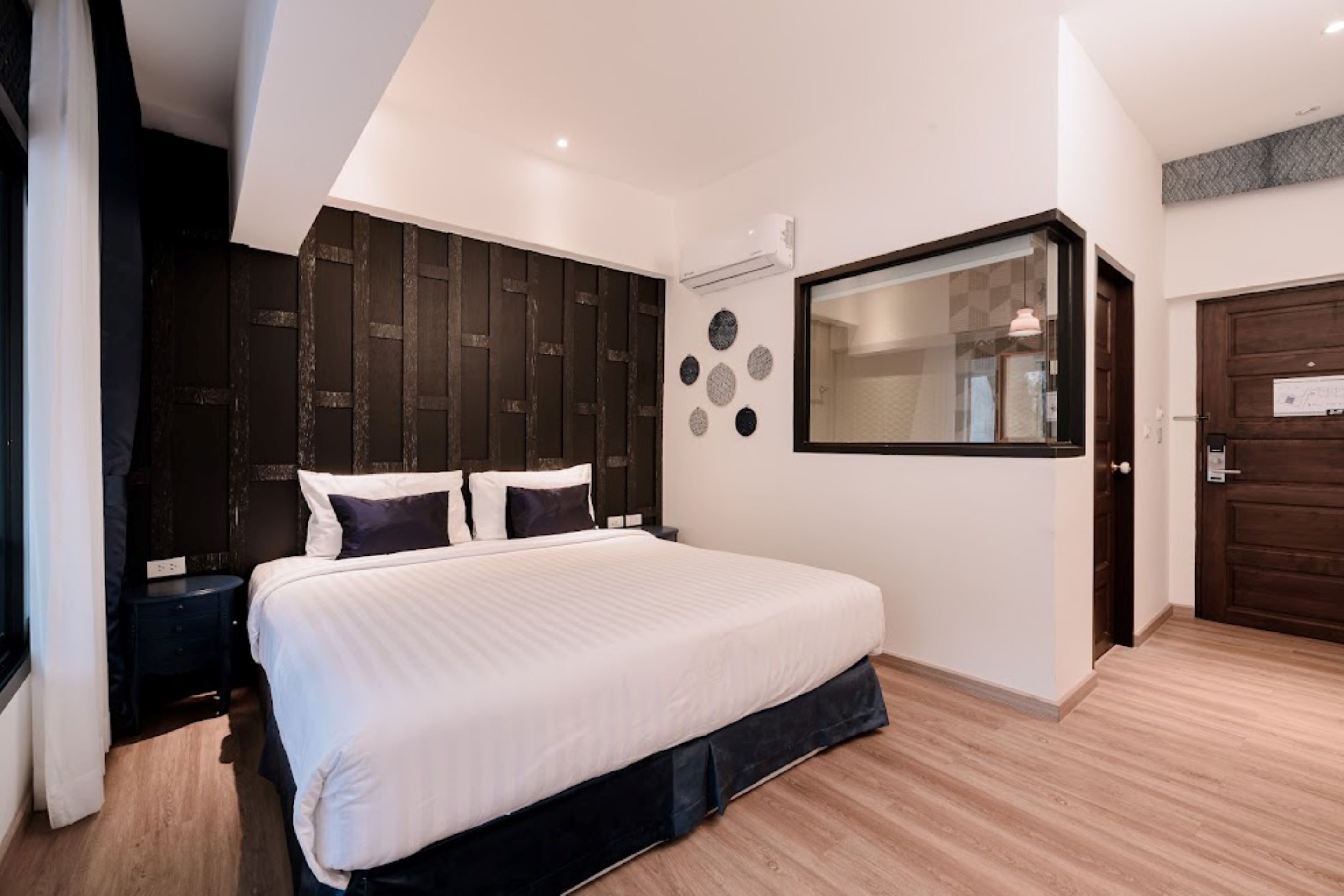 A modern bedroom with a large bed, dark wooden headboard, and a large window.