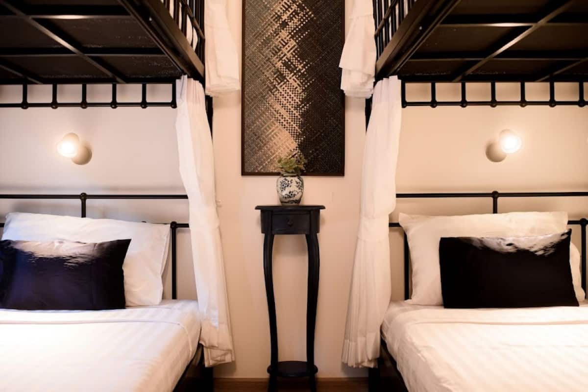 Una habitación con dos camas, una mesita con un florero y una lámpara fijada a la pared.