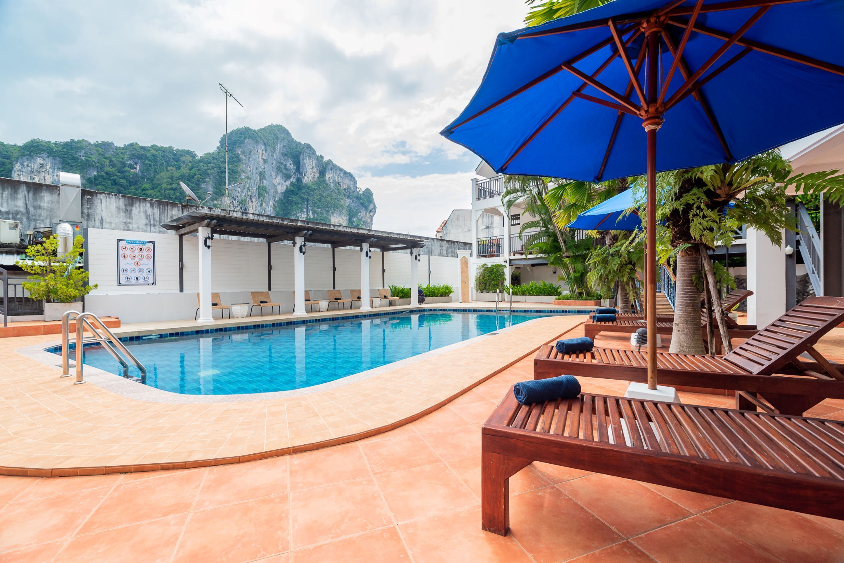 Une piscine entourée de chaises longues et de parasols, avec une terrasse carrelée et une vue imprenable sur les montagnes.