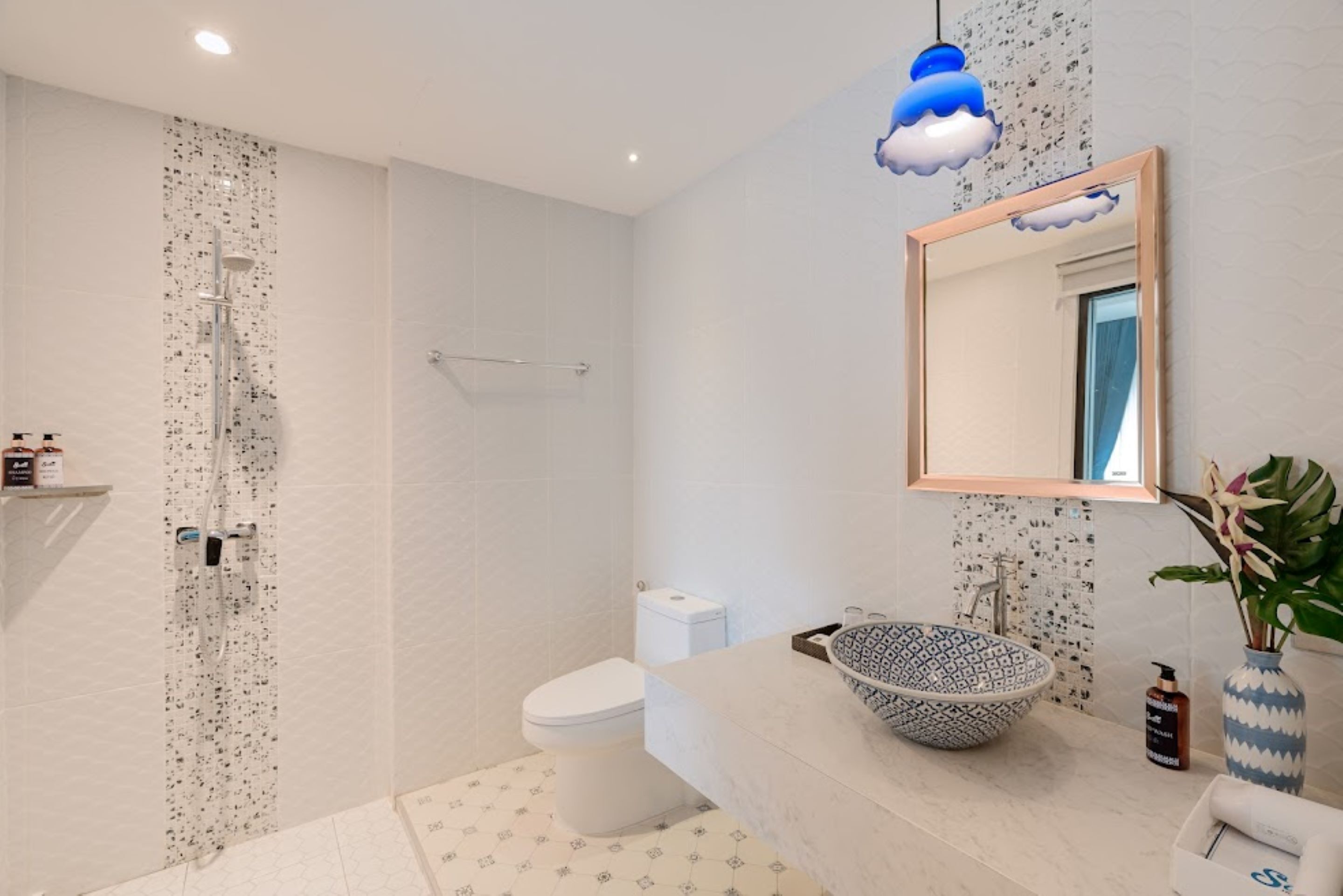 A modern bathroom with a freestanding shower, a toilet, a sink with a patterned bowl, and a mirror with a cloud-shaped light fixture.