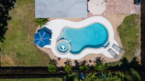 An aerial view of a swimming pool area with a circular water feature, lounge chairs, and umbrellas. - Paradise 4 min to Beach with Heated Pool and Spa (Deerfield Beach)