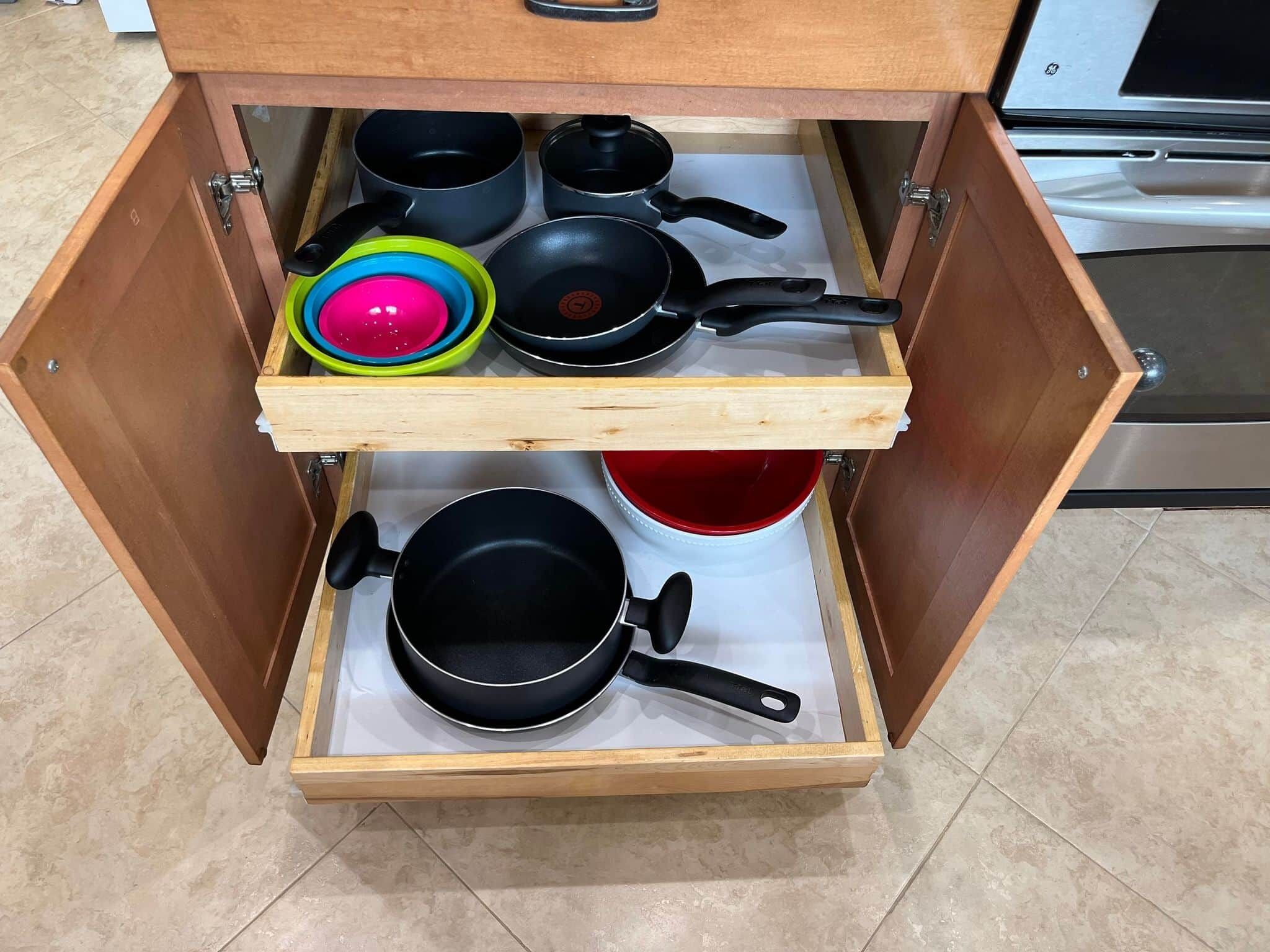 A kitchen drawer with multiple pots and pans, including a red pot and a black pan.