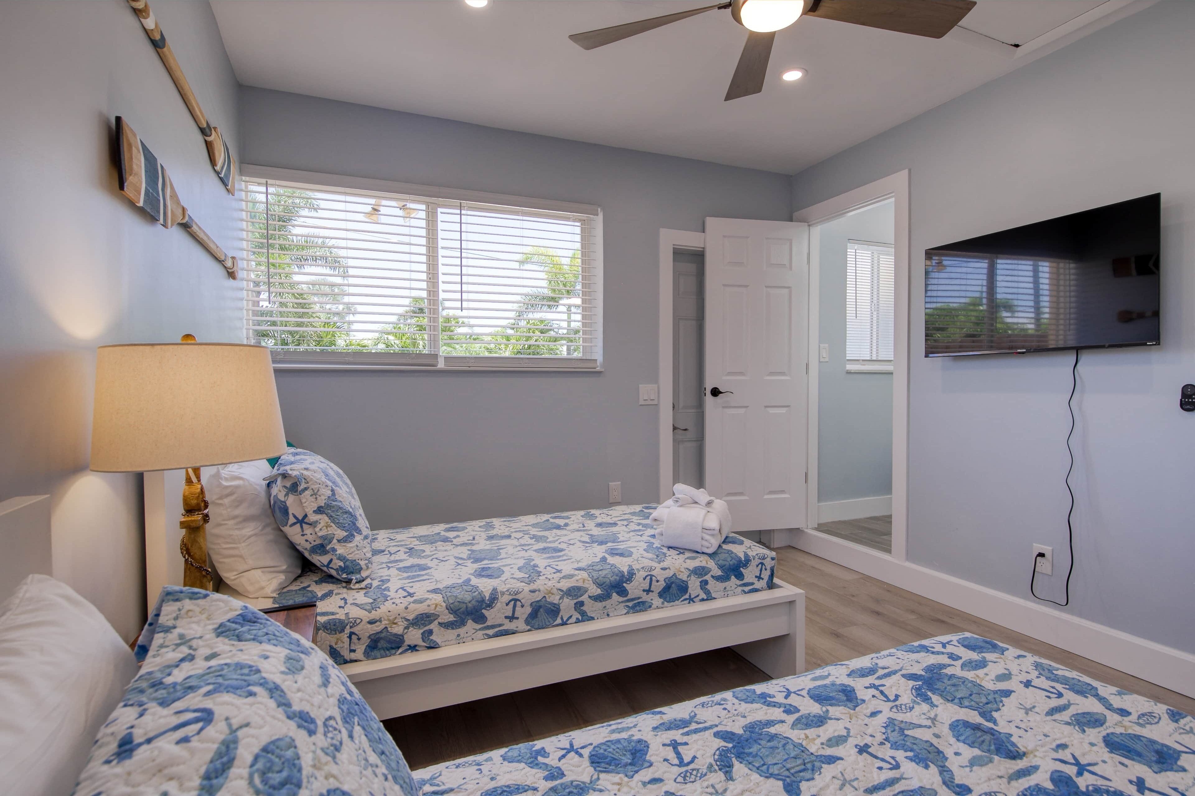 A bedroom with two beds, a ceiling fan, a TV, and a window with blinds.