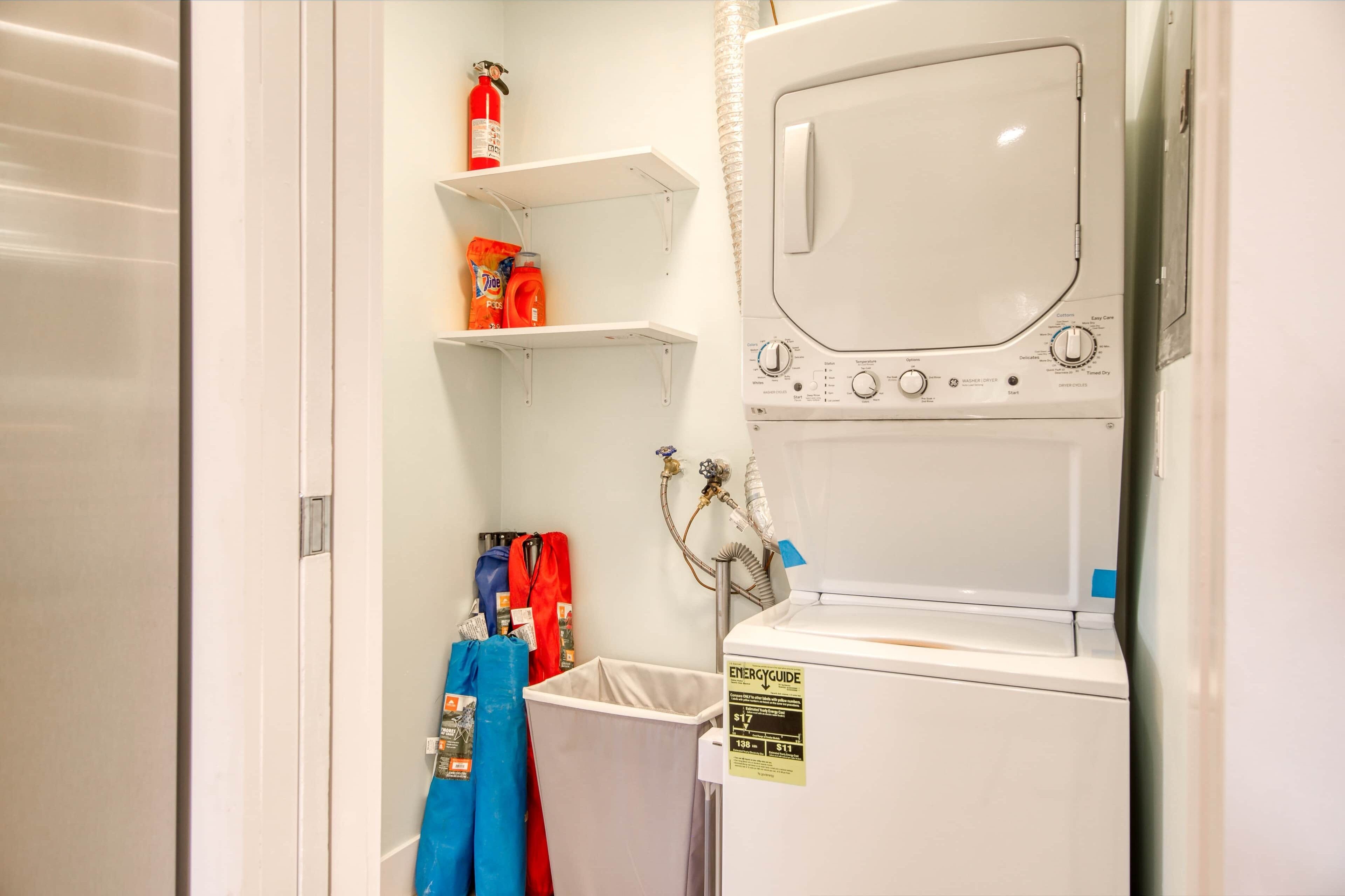 A laundry room with a washing machine, shelves with cleaning supplies, and a fire extinguisher.