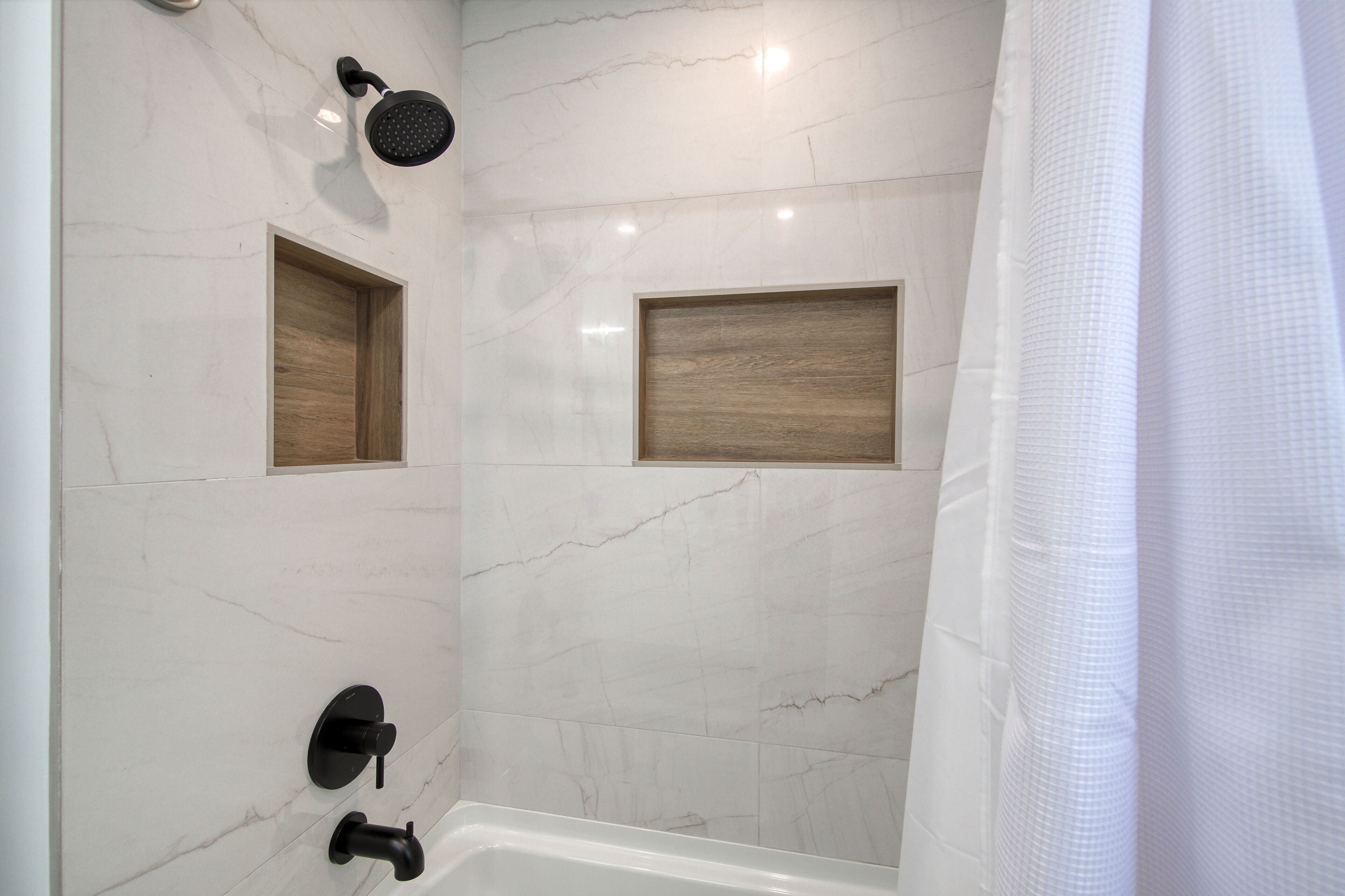A modern bathroom with a shower, a bathtub, and two wooden shelves.