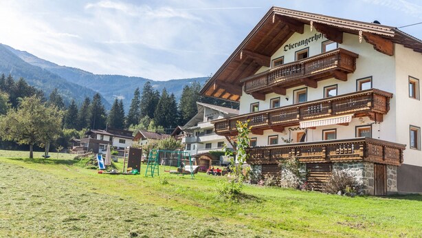A mountain lodge with a wooden balcony, a playground, and a view of the surrounding mountains.