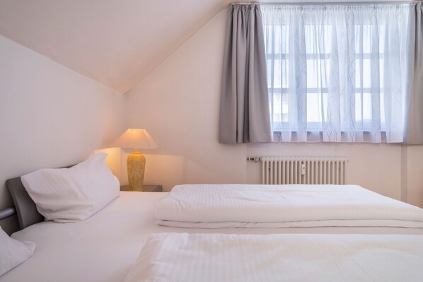 A bedroom with a bed, a nightstand, a lamp, a radiator, and a window with curtains.