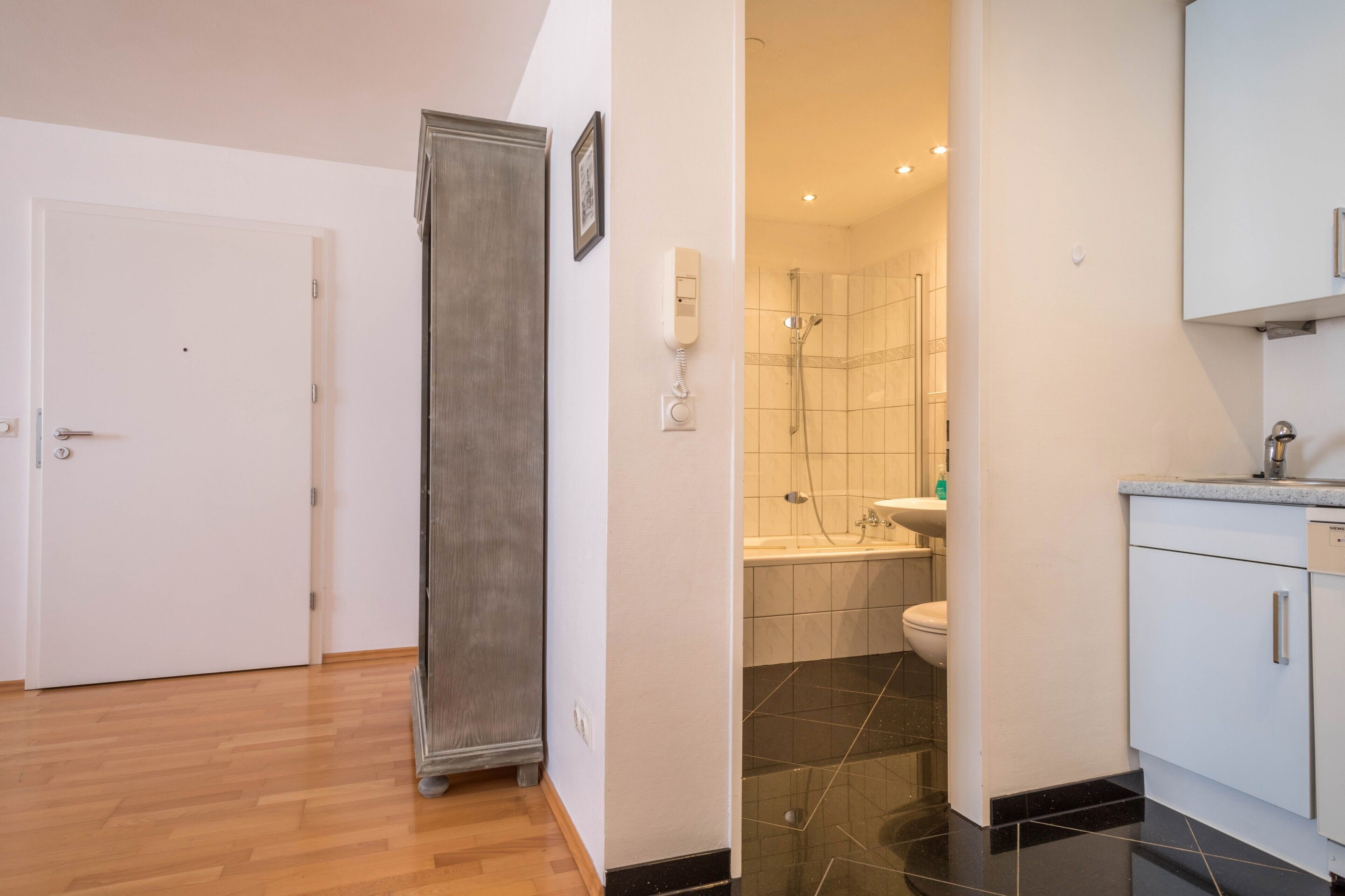 Una camera d'albergo con pavimento in legno, un armadio, un bagno con doccia, un water e un lavandino.
