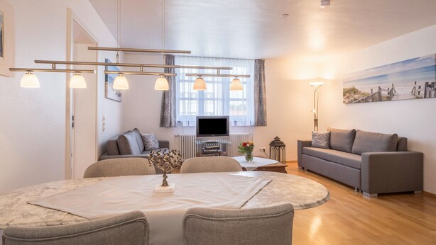 A modern living room with a dining table, sofa, TV, and artwork on the wall. - Holiday Apartment Rathausplatz (Kempten)