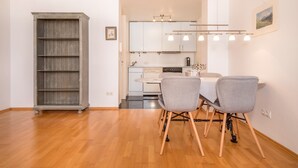 A dining area with a wooden floor, a dining table with chairs, a kitchen in the background, and a bookshelf. - Holiday Apartment Rathausplatz (Kempten)