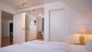 A bedroom with a bed, a nightstand, a lamp, a chair, and a door leading to another room. - Holiday Apartment Rathausplatz (Kempten)