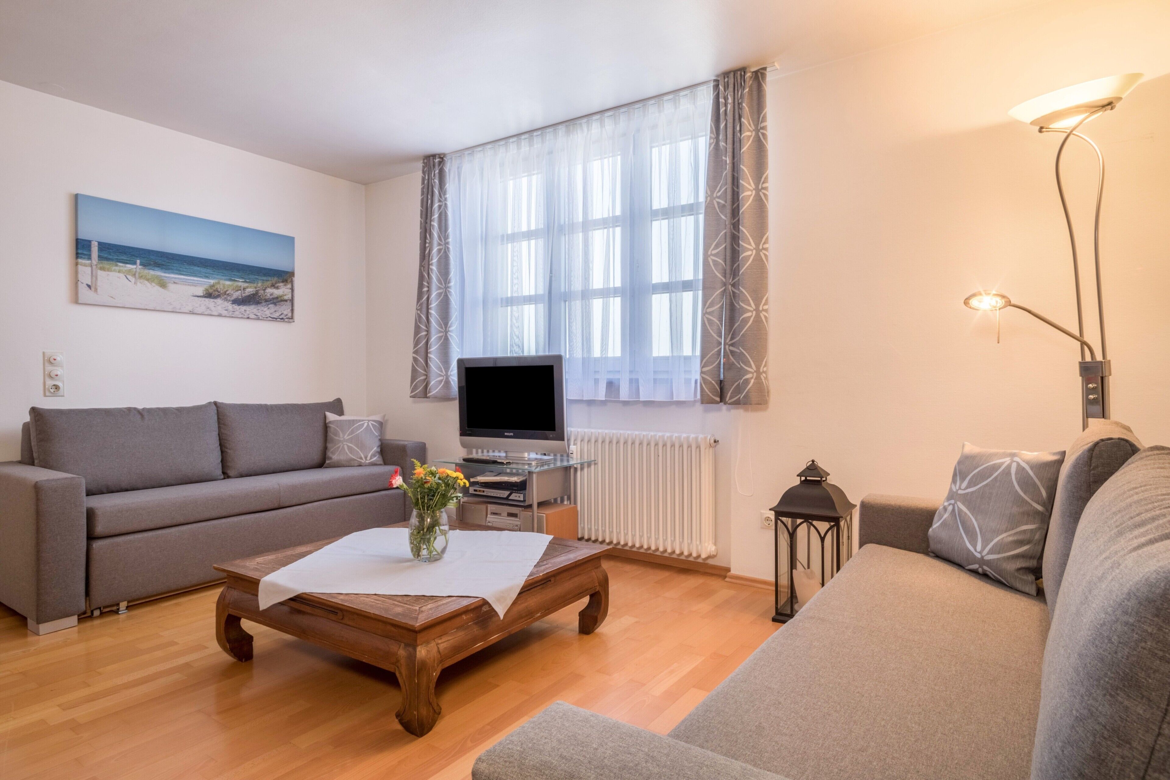 Ett vardagsrum med en soffa, ett soffbord, en tv och ett fönster med gardiner.