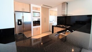 A modern kitchen with stainless steel appliances, a black granite countertop, and light wood cabinetry.