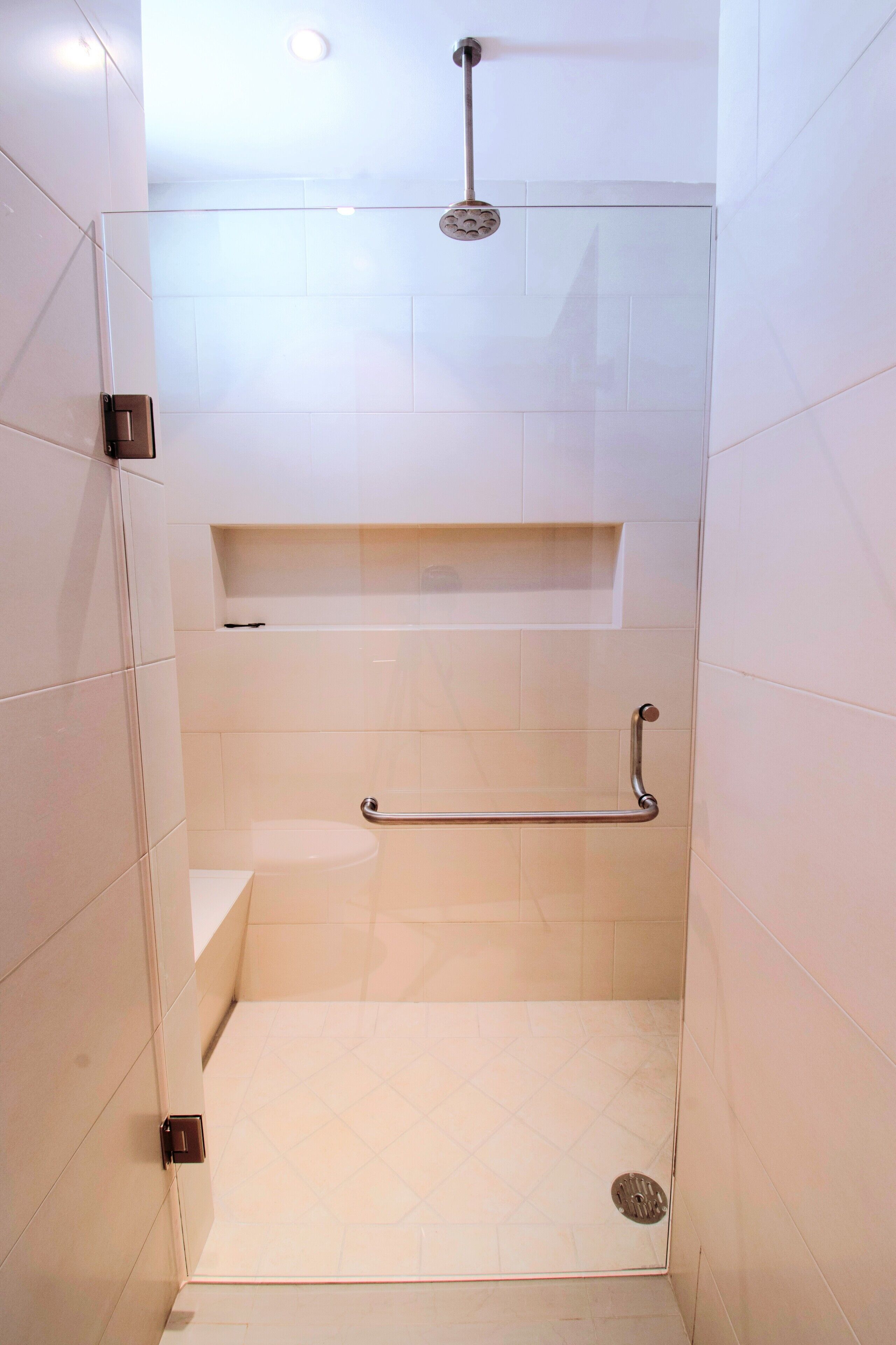 A walk-in shower with a glass door, a handheld showerhead, a grab bar, and a shelf above the toilet.