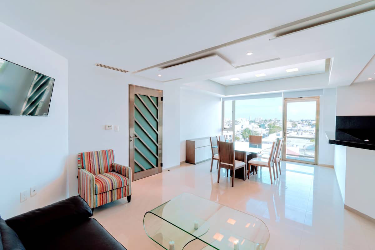 Una sala moderna con una mesa de centro de vidrio, un sillón a rayas y un televisor de pantalla plana montado en la pared.