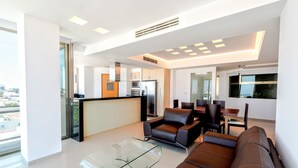 A modern living room with a glass coffee table, leather sofa, and a dining area with chairs.