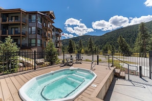 A wooden deck with a hot tub, a fenced area, and a mountain backdrop. - Clearwater Lofts Building 1 by Summit County Mountain Retreats (Keystone)