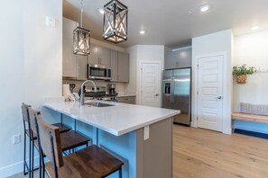 Uma cozinha moderna com ilha central, eletrodomésticos de aço inoxidável e iluminação pendente.