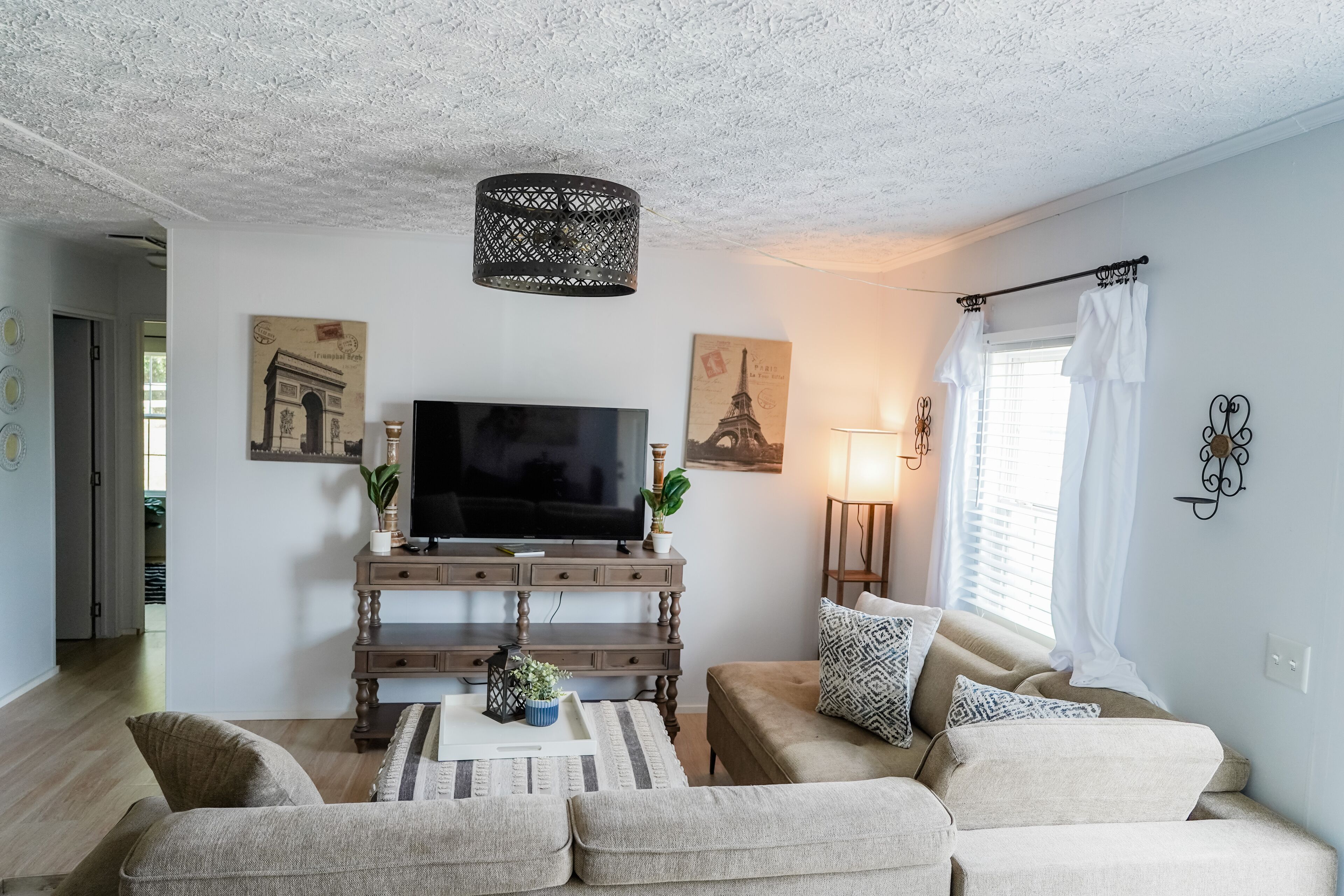 En stue med et fladskærms-tv, et tv-møbel i træ, en beige sofa og en pude med mønster.