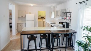 A modern kitchen with a central island, bar stools, and a view into the dining area. - The Cozy Retreat - 3BR - Sleeps 7 - Near Greenville Mauldin & Simpsonville (Greenville)