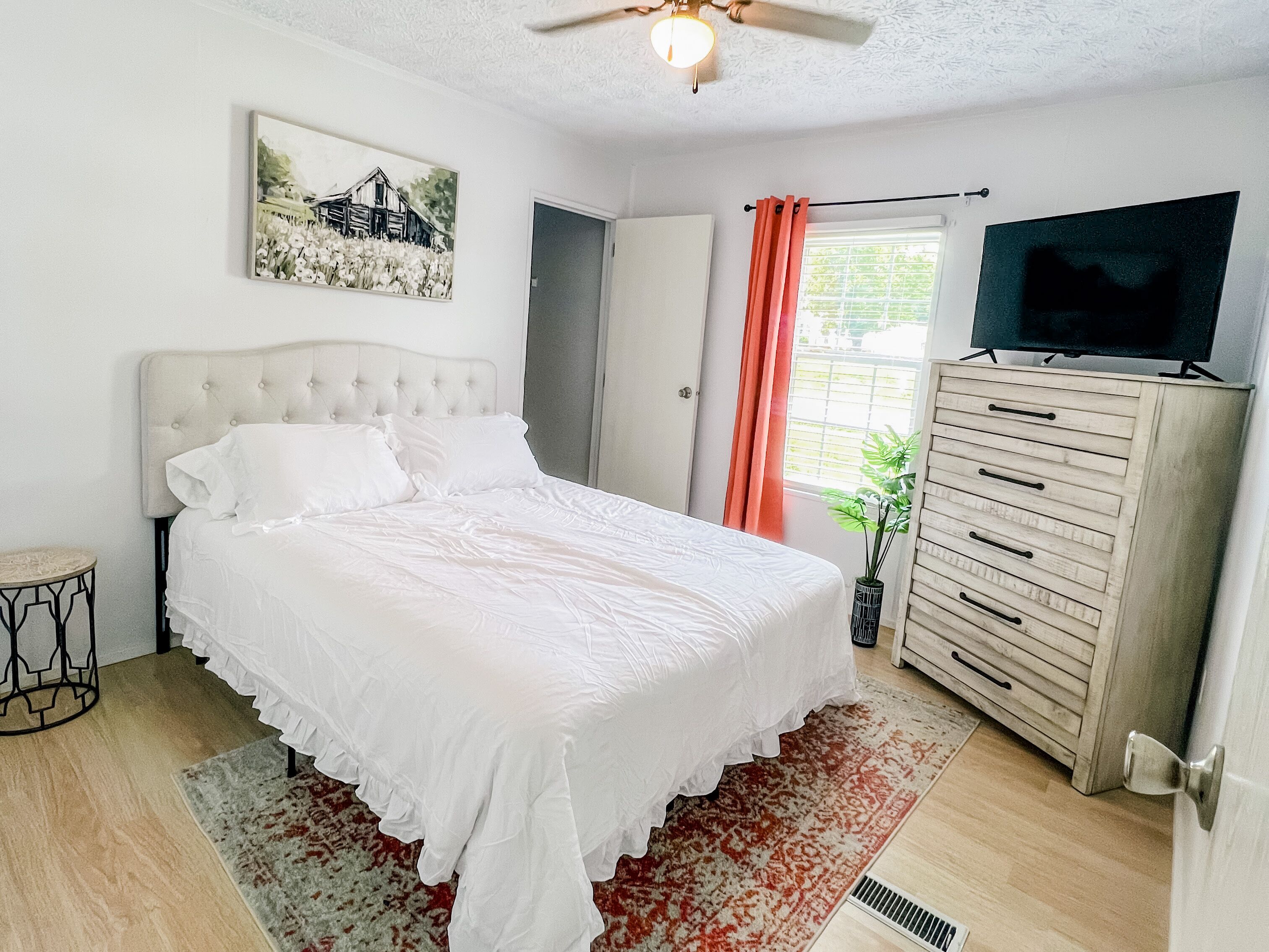 Een slaapkamer met een bed, een dressoir, een televisie en een schilderij aan de muur.