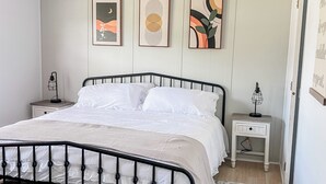 A neatly made bed with a black metal frame, white bedding, and a patterned rug. There are two bedside tables with lamps, and three framed artworks on the wall. - The Cozy Retreat - 3BR - Sleeps 7 - Near Greenville Mauldin & Simpsonville (Greenville)