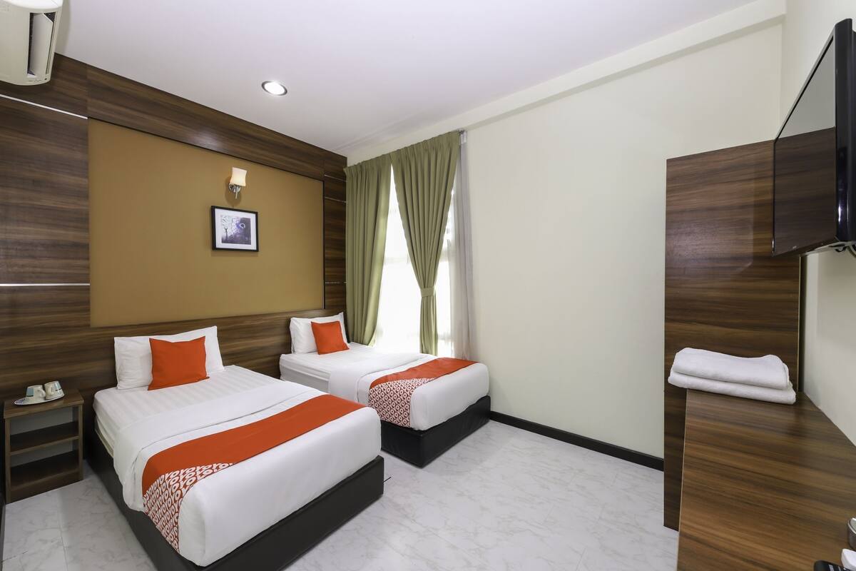 Une chambre d’hôtel avec deux lits, un téléviseur à écran plat, un mur décoratif en bois, un tableau et une fenêtre avec des rideaux.