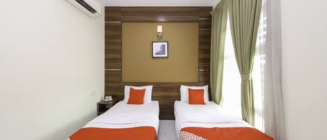 Habitación de hotel con dos camas individuales, una mesita de noche, un equipo de aire acondicionado, un cuadro en la pared y una ventana con cortinas.