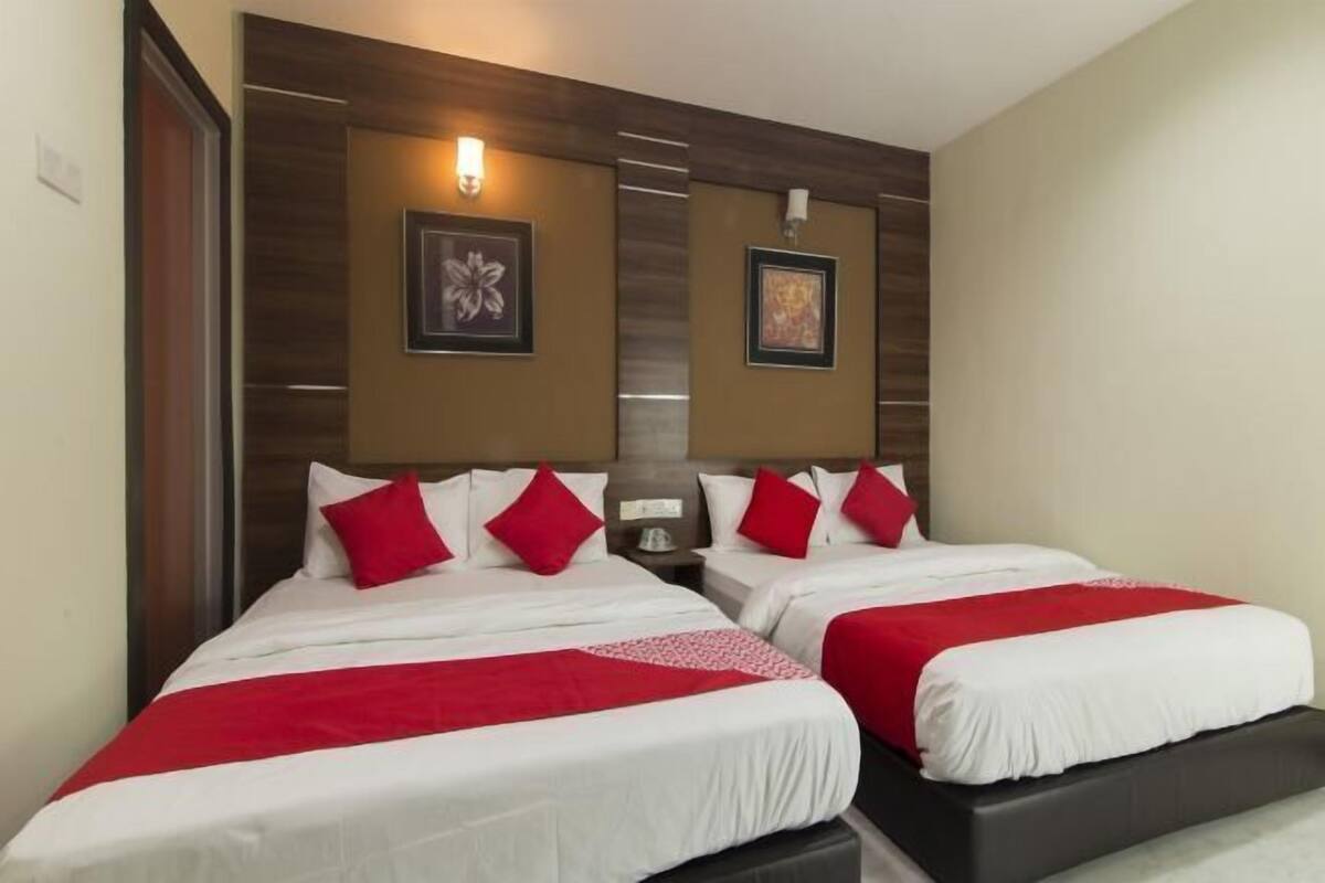Une chambre d’hôtel avec deux lits, chacun agrémenté de draps rouges et blancs, d’une tête de lit en bois et de deux tableaux encadrés accrochés au mur.