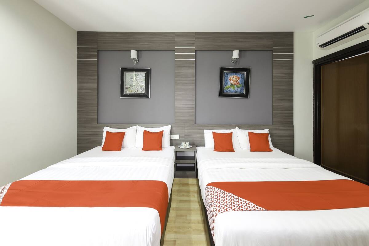 Une chambre d’hôtel avec deux lits, chacun agrémenté de draps blancs et orange, et deux œuvres d’art encadrées accrochées au mur.