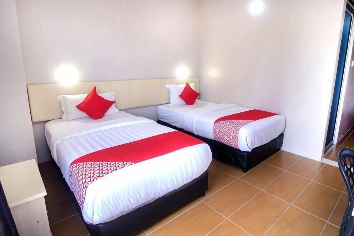 Une chambre d’hôtel avec deux lits, chacun agrémenté de draps blancs et de touches de couleur rouge, un plancher en bois et une table de chevet.