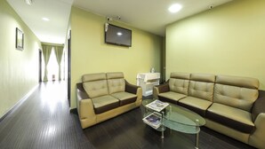 A hotel lobby with two leather sofas, a glass coffee table, a flat-screen TV mounted on the wall, and a reception desk. - Collection O Shah Alam Formerly Hotel SMC Seksyen 13 (Shah Alam)