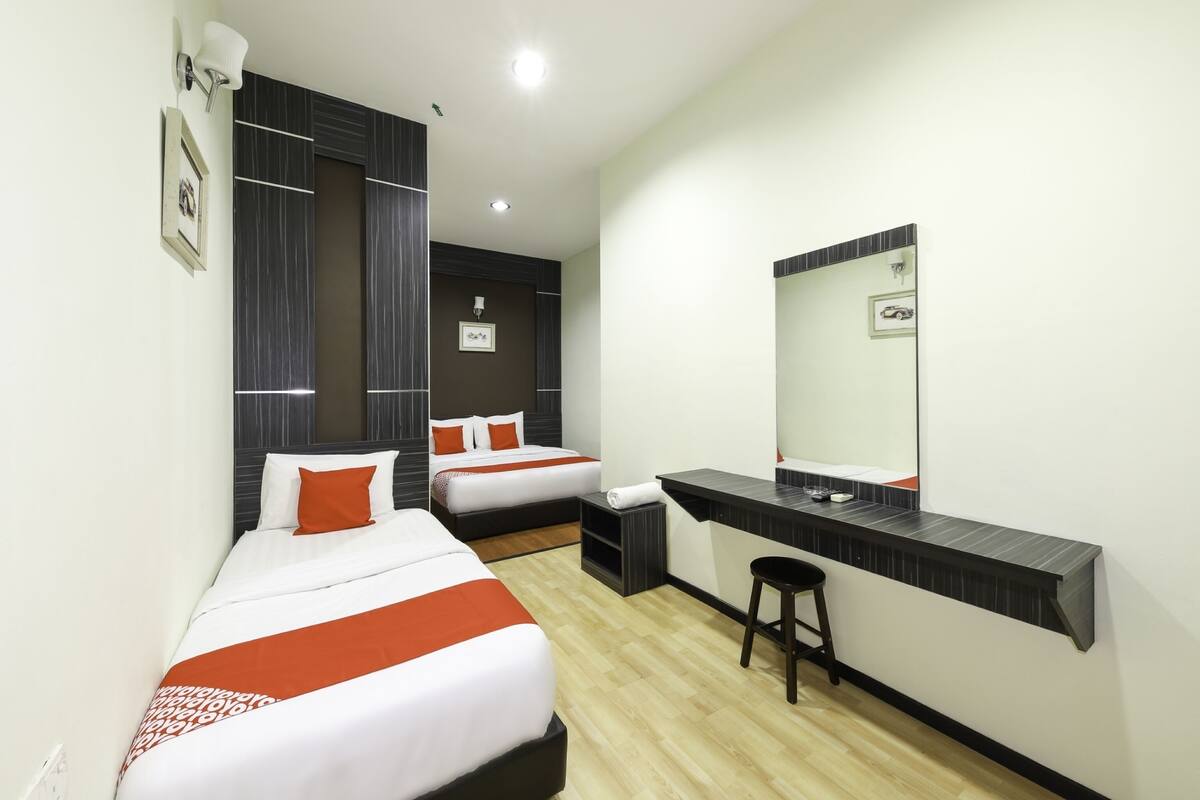 Une chambre d’hôtel avec deux lits, un bureau, un miroir et un petit tabouret.