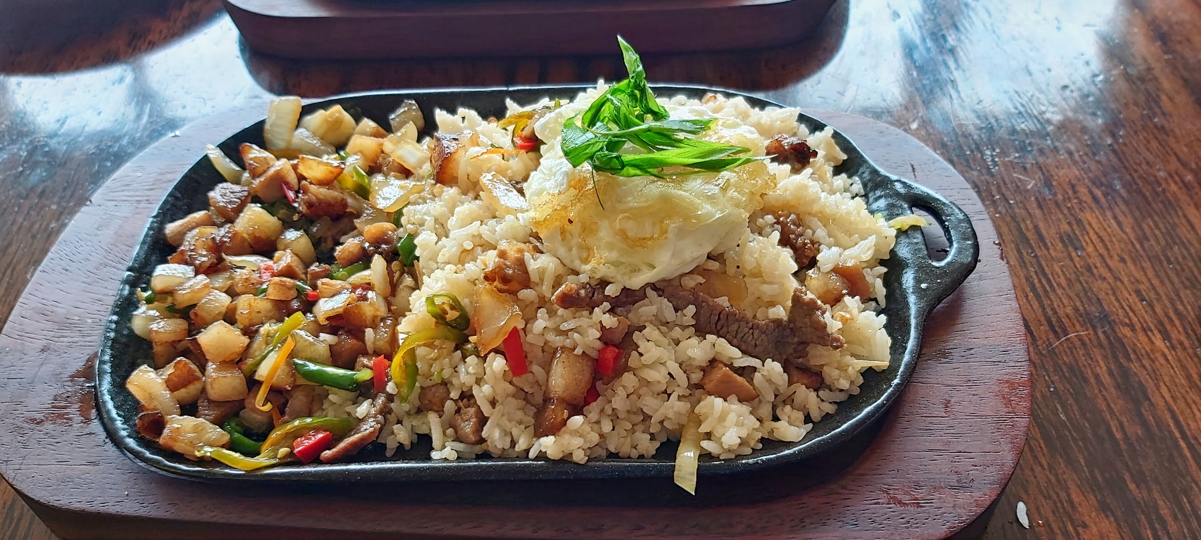 A plate of fried rice with vegetables and meat, garnished with green herbs, served on a black plate.