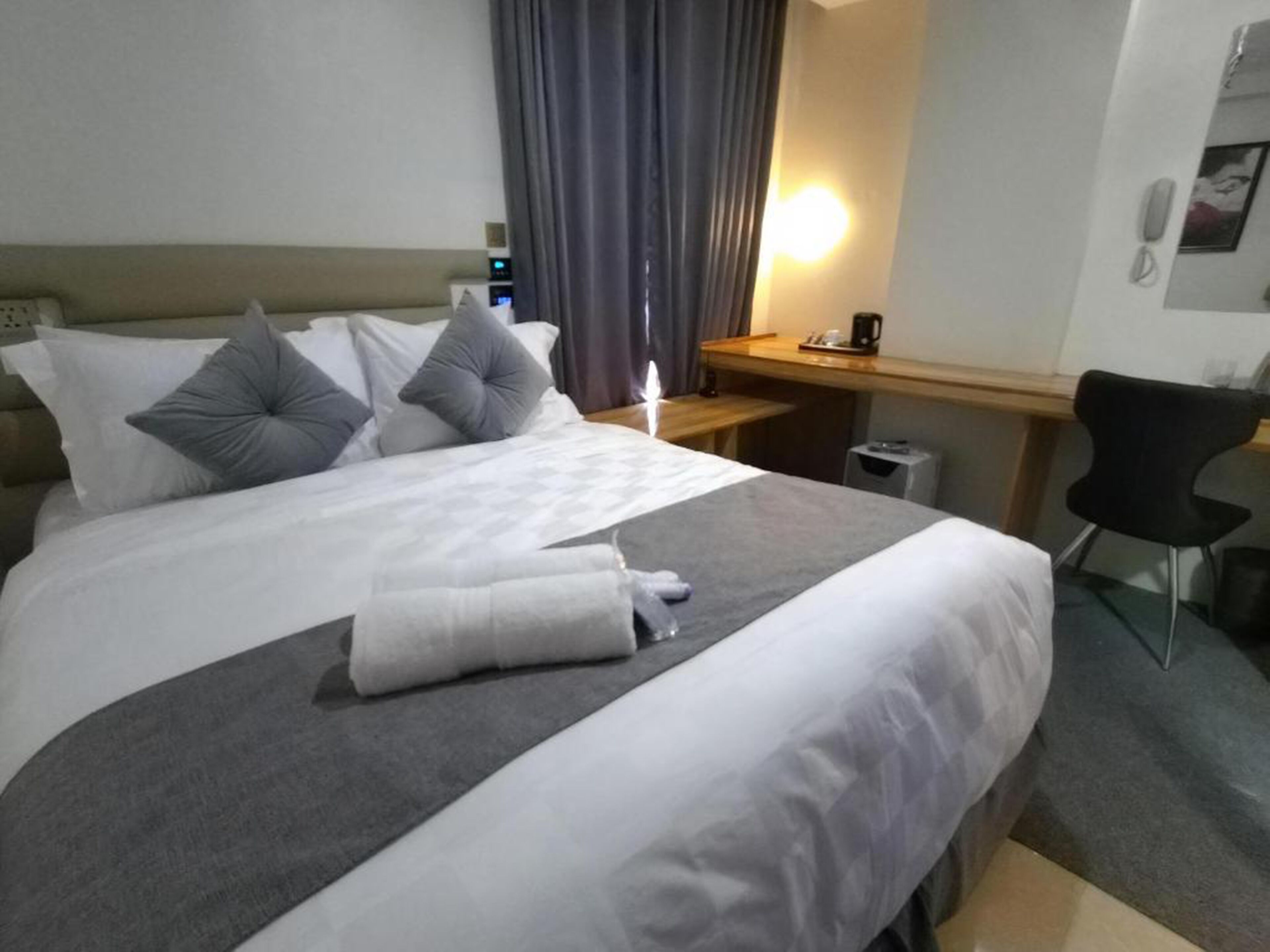 A hotel room with a bed, pillows, a desk, a chair, and a nightstand.