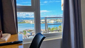 Ein Hotelzimmer mit großem Fenster, das Blick auf ein Gewässer, eine Brücke und entfernte Gebäude bietet.
