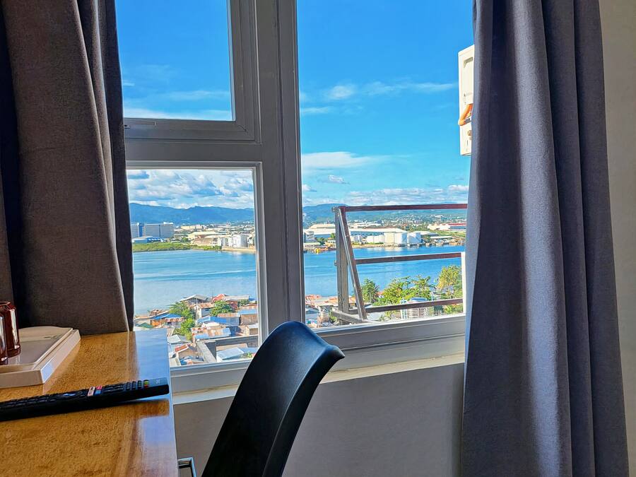Une chambre d’hôtel dotée d’une grande fenêtre donnant sur un plan d’eau, un pont et des bâtiments situés au loin.