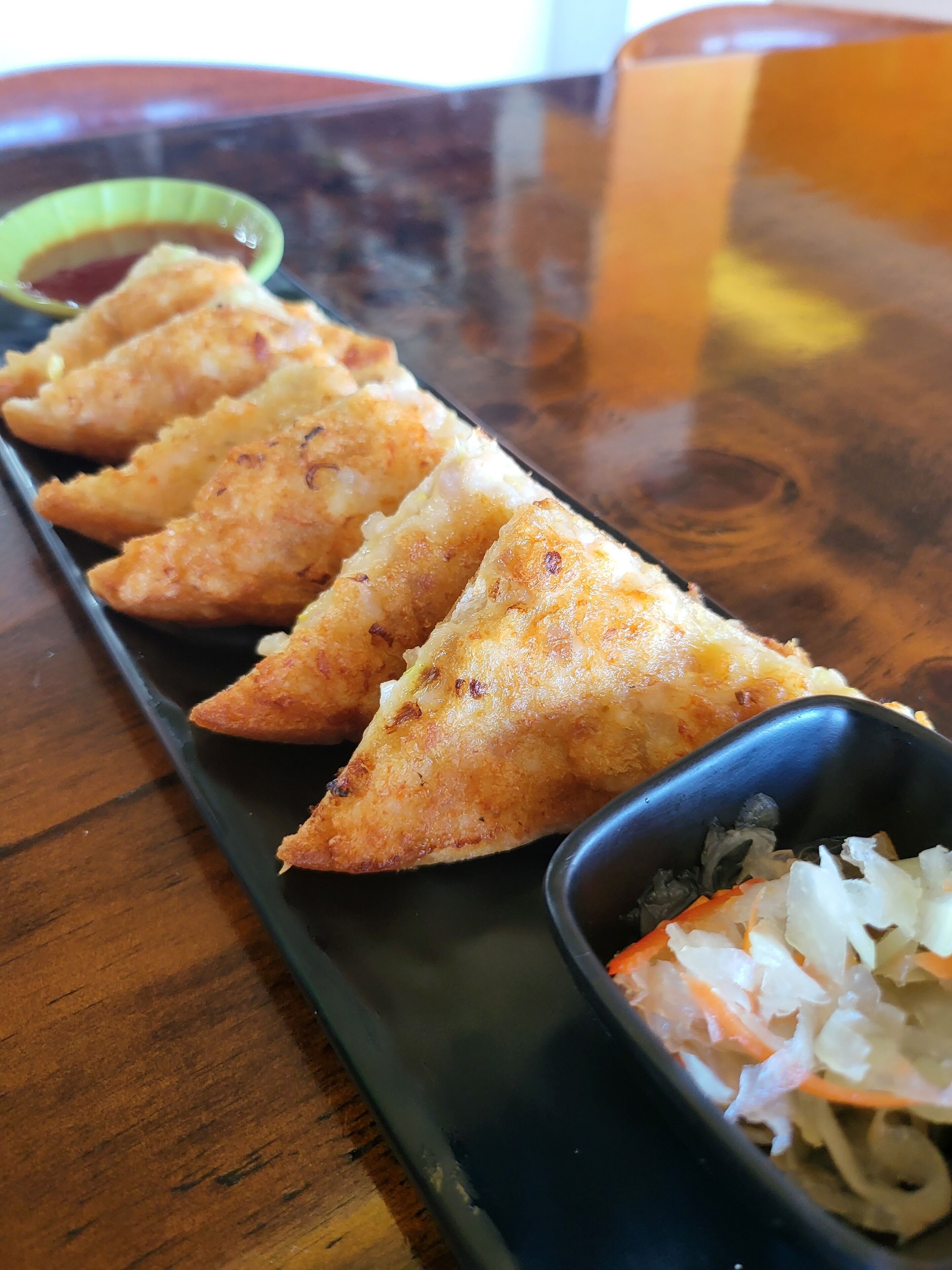 A tray with four triangular pastries and a small bowl of shredded vegetables.