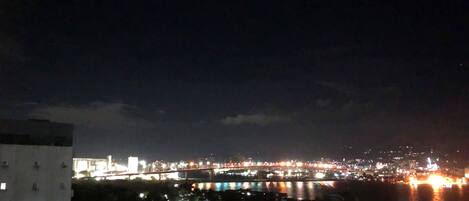 Un paisaje urbano nocturno con un río, un puente iluminado y edificios a lo largo de la ribera.