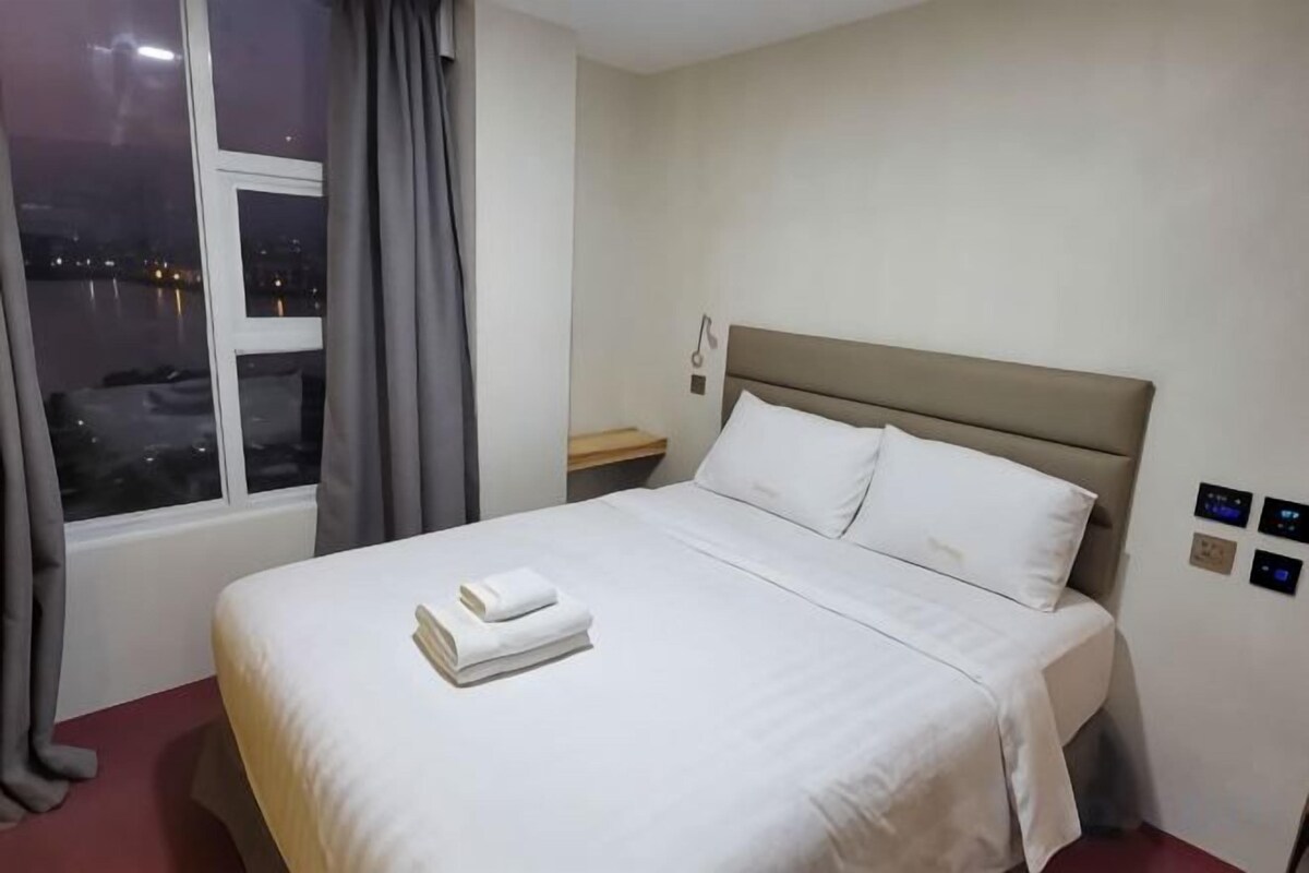 Een hotelkamer met een bed, een nachtkastje, een raam met gordijnen en een uitzicht op de stad 's nachts.