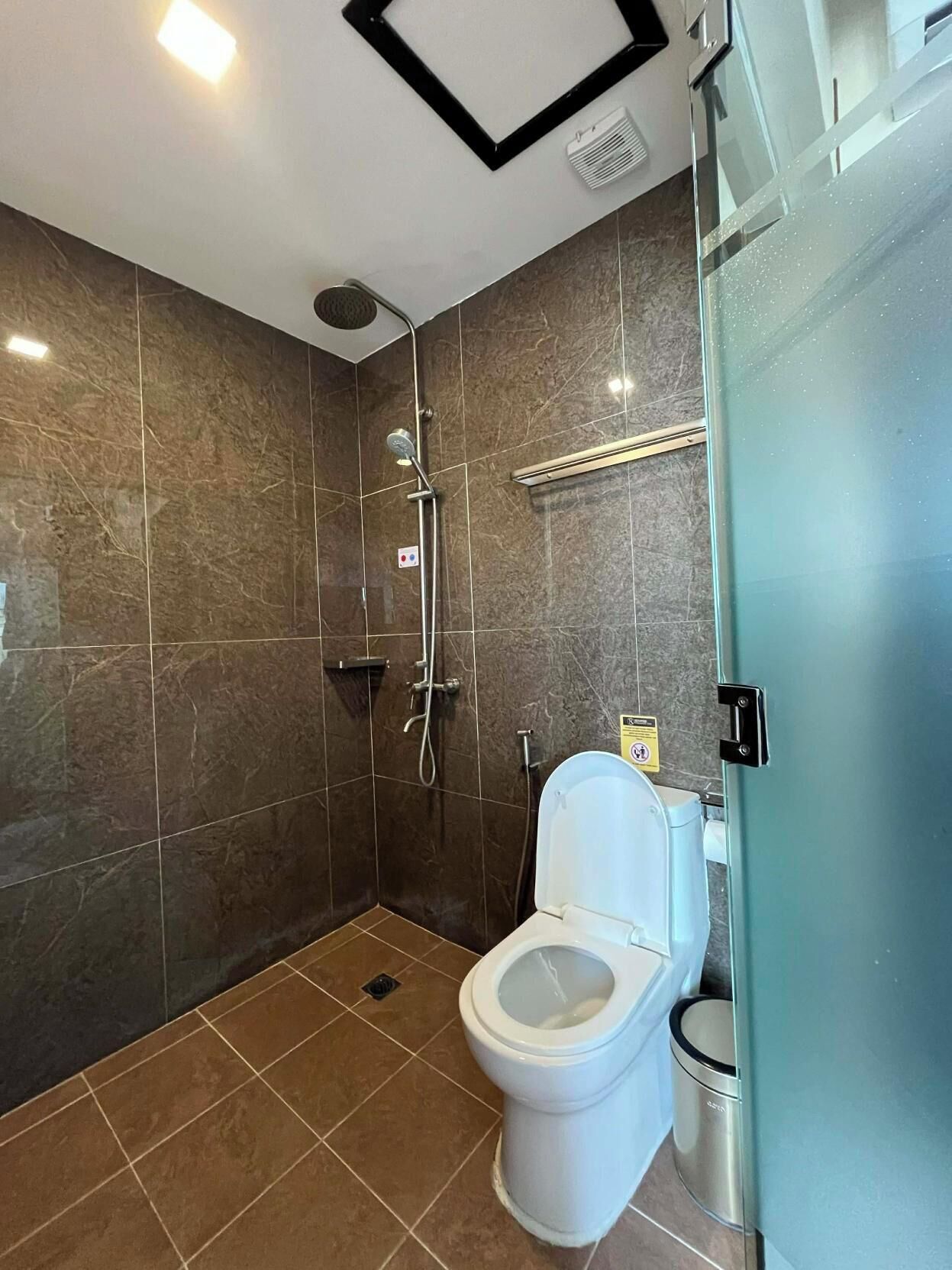 A modern bathroom with a shower, toilet, and a glass partition.