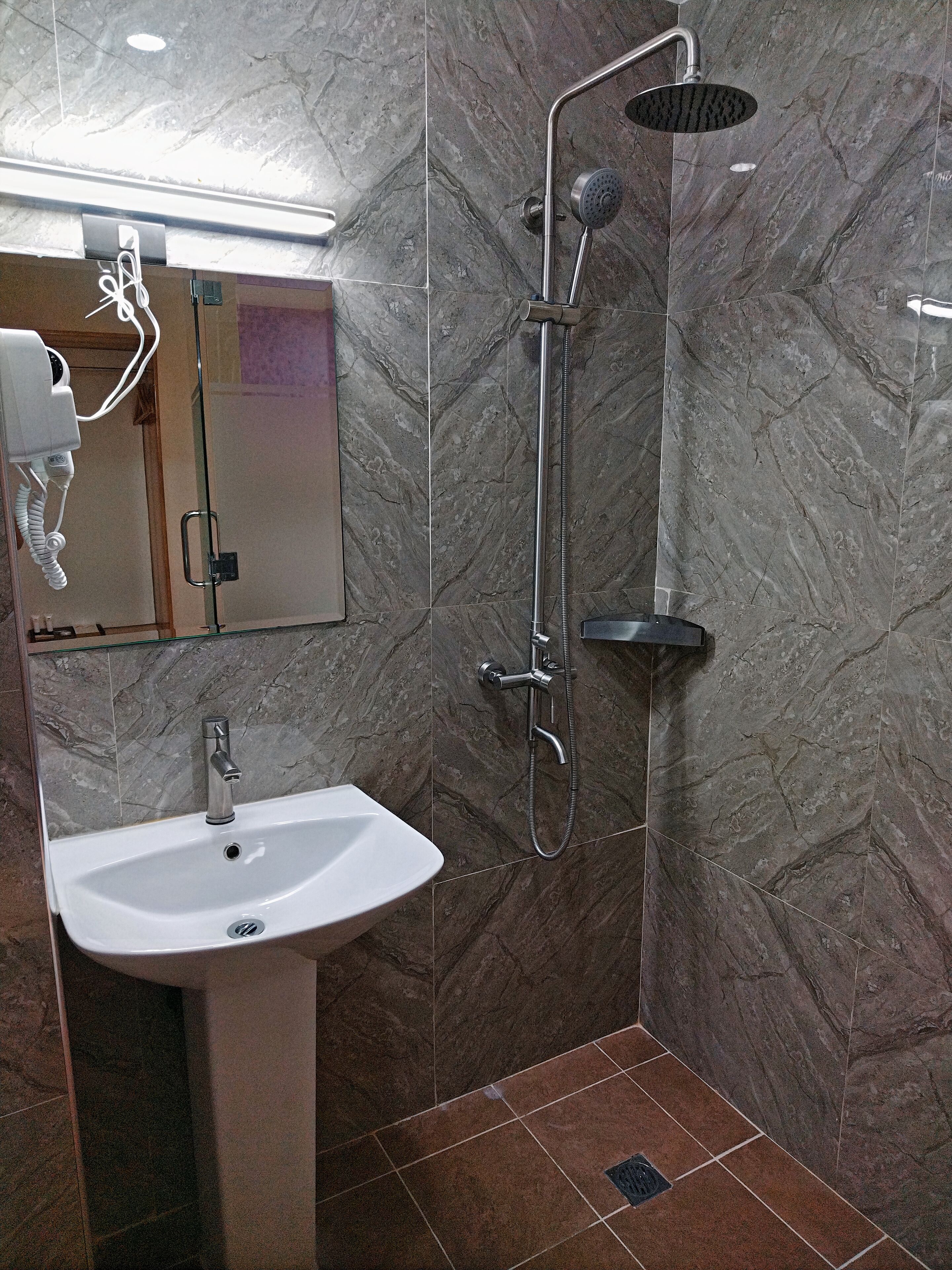 Ein Badezimmer mit Marmorwand, Waschbecken und Dusche mit Duschbrause.