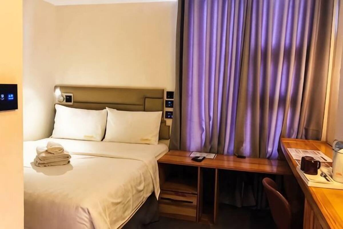 Une chambre d’hôtel comprenant un lit, une table de chevet, un bureau, une chaise et des rideaux.