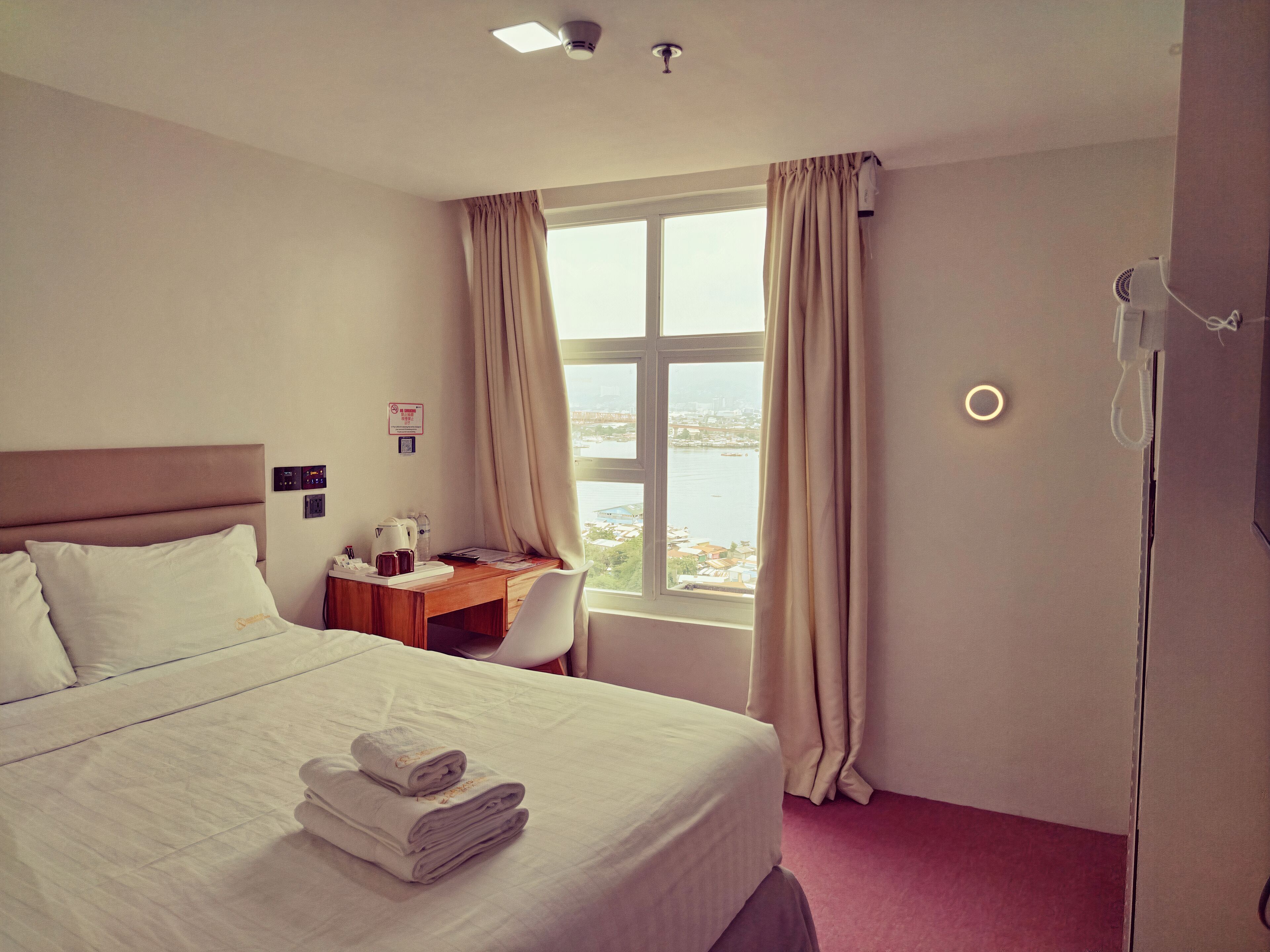 Habitación de hotel con cama, escritorio, silla, ventana con cortinas y vistas a la ciudad.