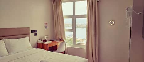 Habitación de hotel con cama, escritorio, silla, ventana con cortinas y vistas a la ciudad.