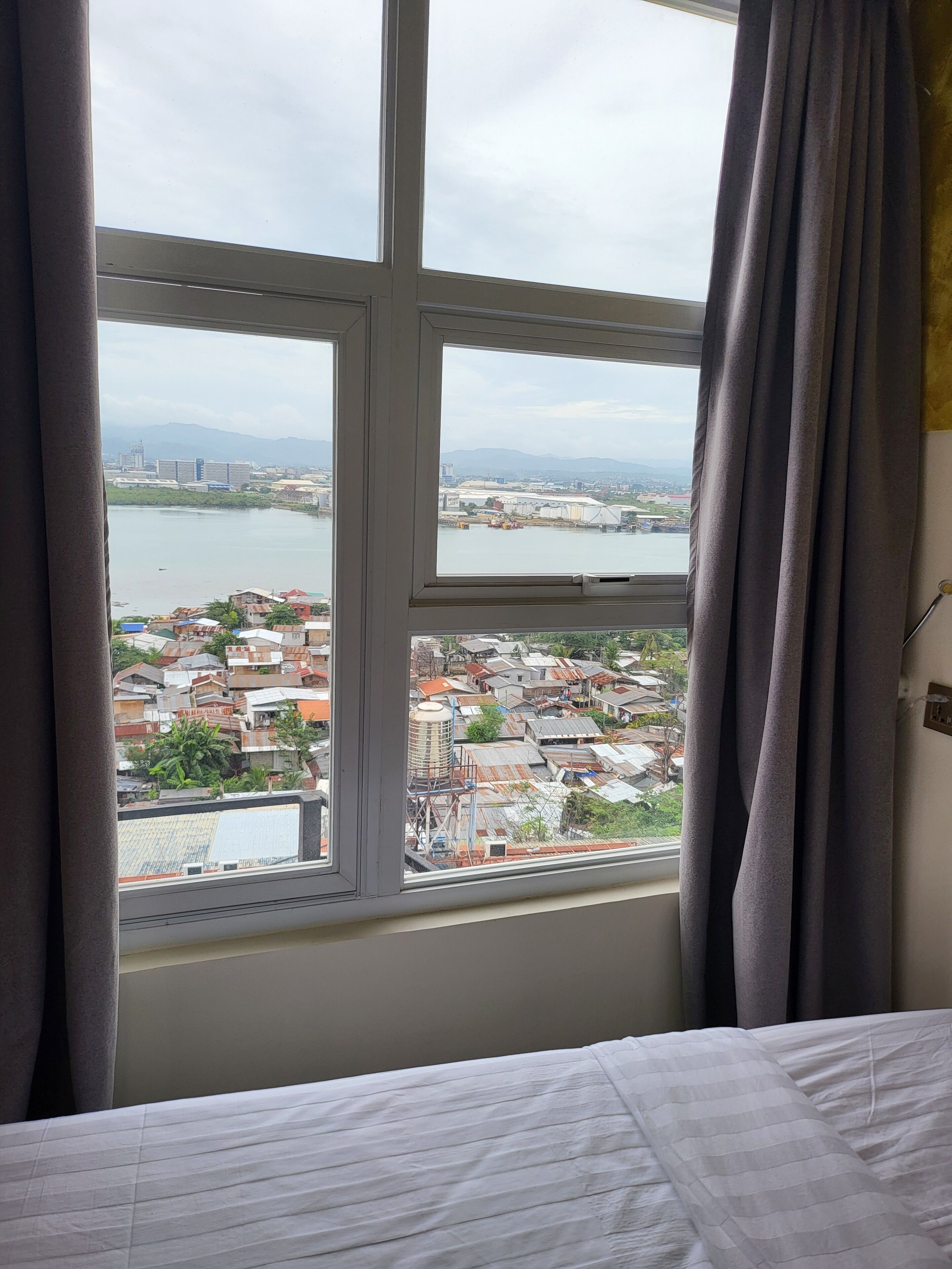 Una habitación con un amplio ventanal que ofrece vistas a un paisaje urbano, que incluye una masa de agua y montañas al lejano.