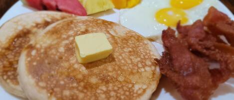 A breakfast plate with pancakes, eggs, bacon, butter, and fruit.