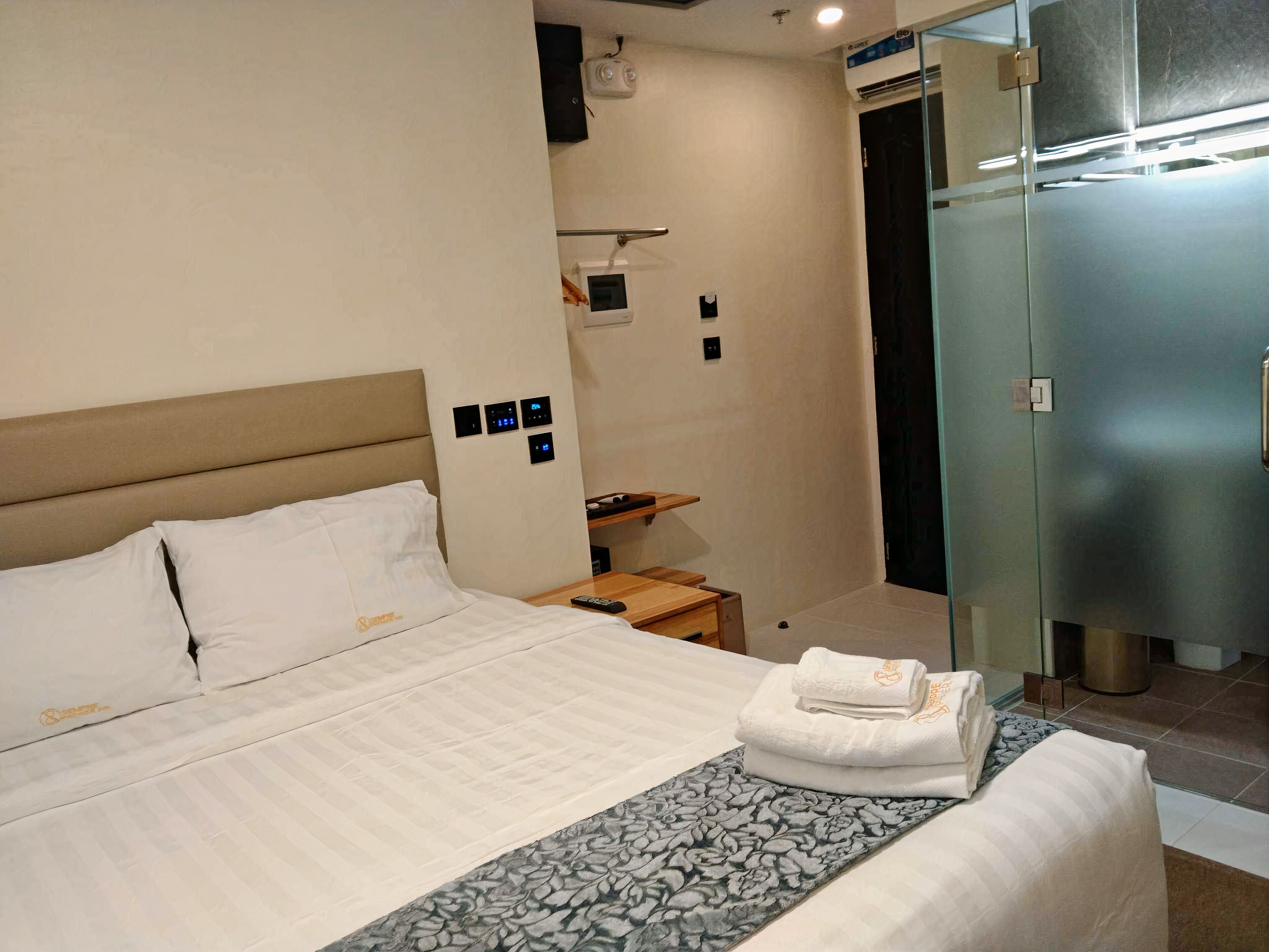 A hotel room with a bed, a bedside table, a mirror, a wardrobe, and a thermostat on the wall.
